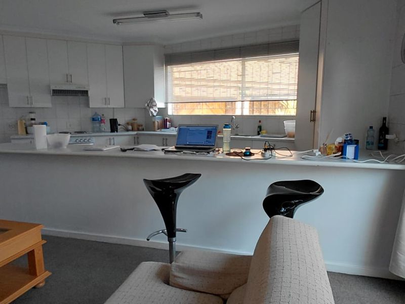 Open plan living area featuring a functional kitchen with white cabinetry, breakfast bar, and tiled splashback, seamlessly connecting to the living space.