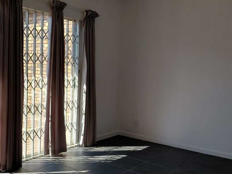 An empty living room featuring dark tiled flooring and sliding glass doors with security gates, providing direct access to the outdoor area.