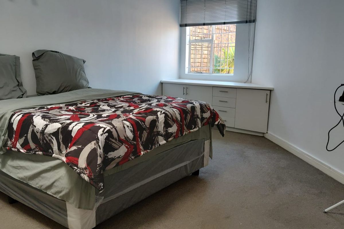 A bedroom featuring neutral walls, carpeted flooring, and built-in storage cabinetry beneath a window with security bars.