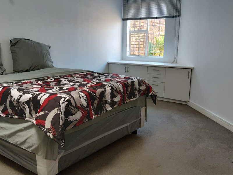 A bedroom featuring neutral walls, carpeted flooring, and built-in storage cabinetry beneath a window with security bars.