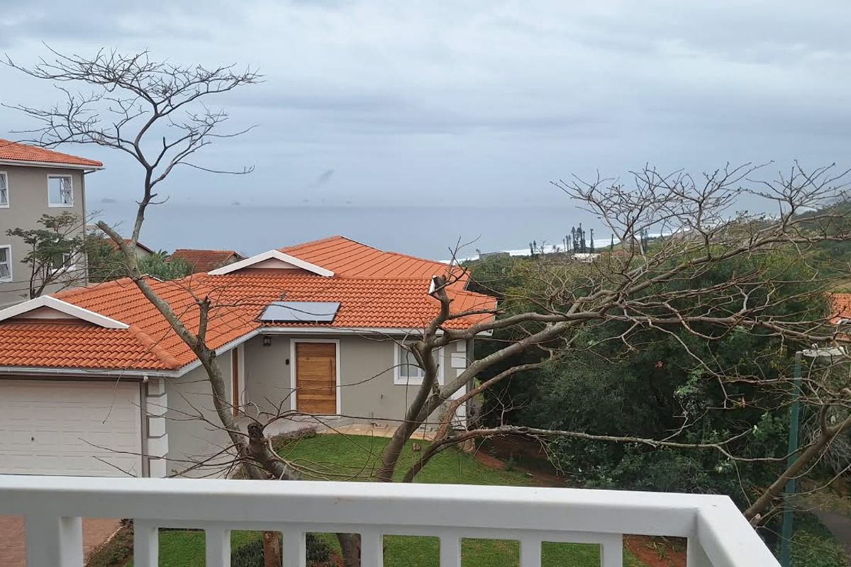 Elevated view overlooking a residential townhouse complex with terracotta tiled roofs, featuring a distant ocean horizon and surrounding coastal landscape.