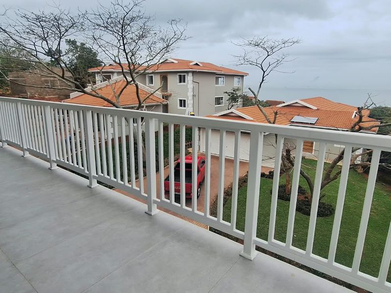 A spacious balcony featuring tiled flooring and a white metal balustrade, offering elevated views of the surrounding estate and coastal landscape.