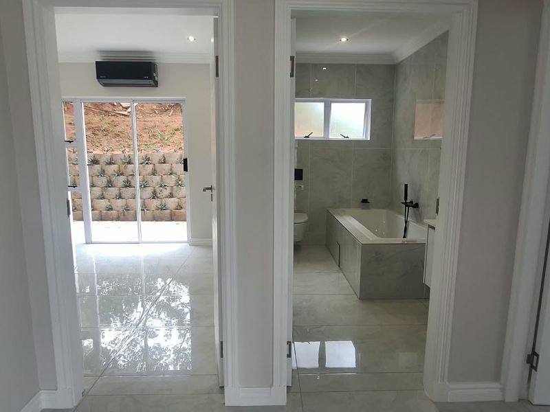 A bright, modern hallway featuring polished tiled flooring, clean white finishes, and direct access to a bathroom and an adjacent living space.