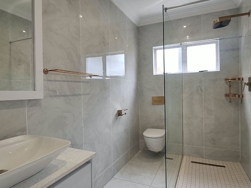 Modern bathroom featuring a walk-in shower with glass screen, wall-mounted toilet, vessel sink on a stone vanity, and contemporary rose gold fixtures.