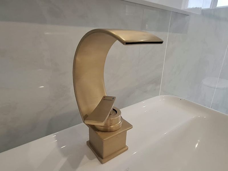 A modern bathroom featuring a stylish gold waterfall basin mixer tap set against elegant marble-look wall tiles.