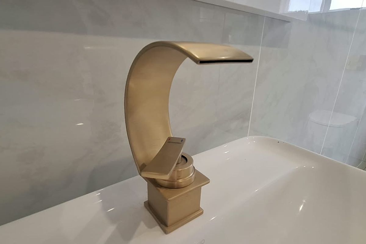 A modern bathroom featuring a stylish gold waterfall basin mixer tap set against elegant marble-look wall tiles.