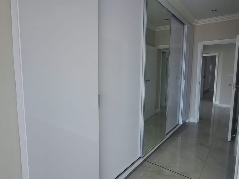 A bright hallway featuring modern built-in sliding door cupboards with mirrored panels and polished tiled flooring.