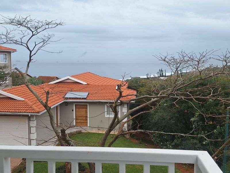 Elevated view overlooking a residential townhouse complex with terracotta tiled roofs, featuring a distant ocean horizon and surrounding coastal landscape.