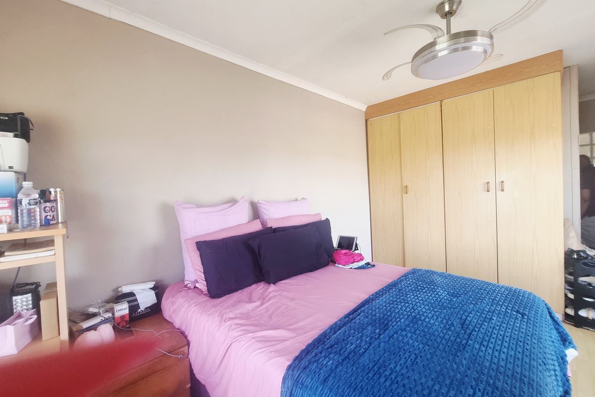 A bedroom featuring built-in wooden cupboards and a modern ceiling fan, providing functional storage and climate control.