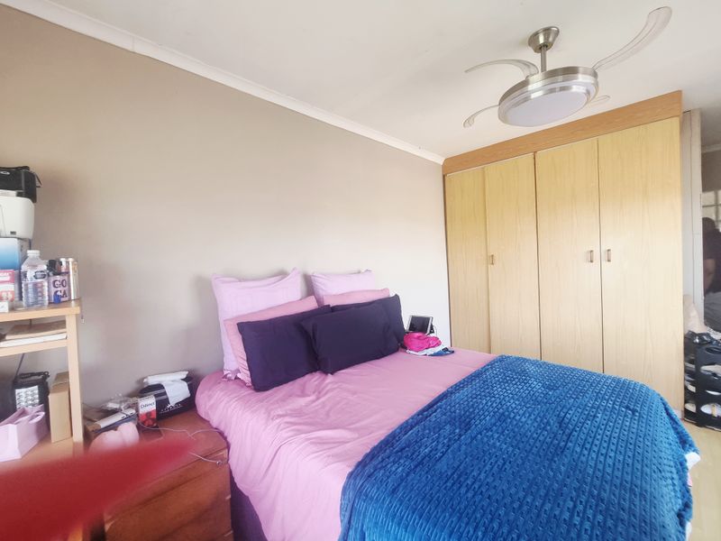 A bedroom featuring built-in wooden cupboards and a modern ceiling fan, providing functional storage and climate control.