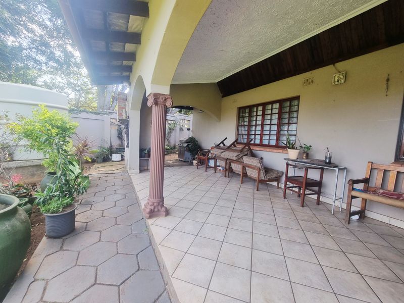 A covered patio area featuring tiled flooring, decorative columns, and timber ceiling beams, providing a functional outdoor space for relaxation.