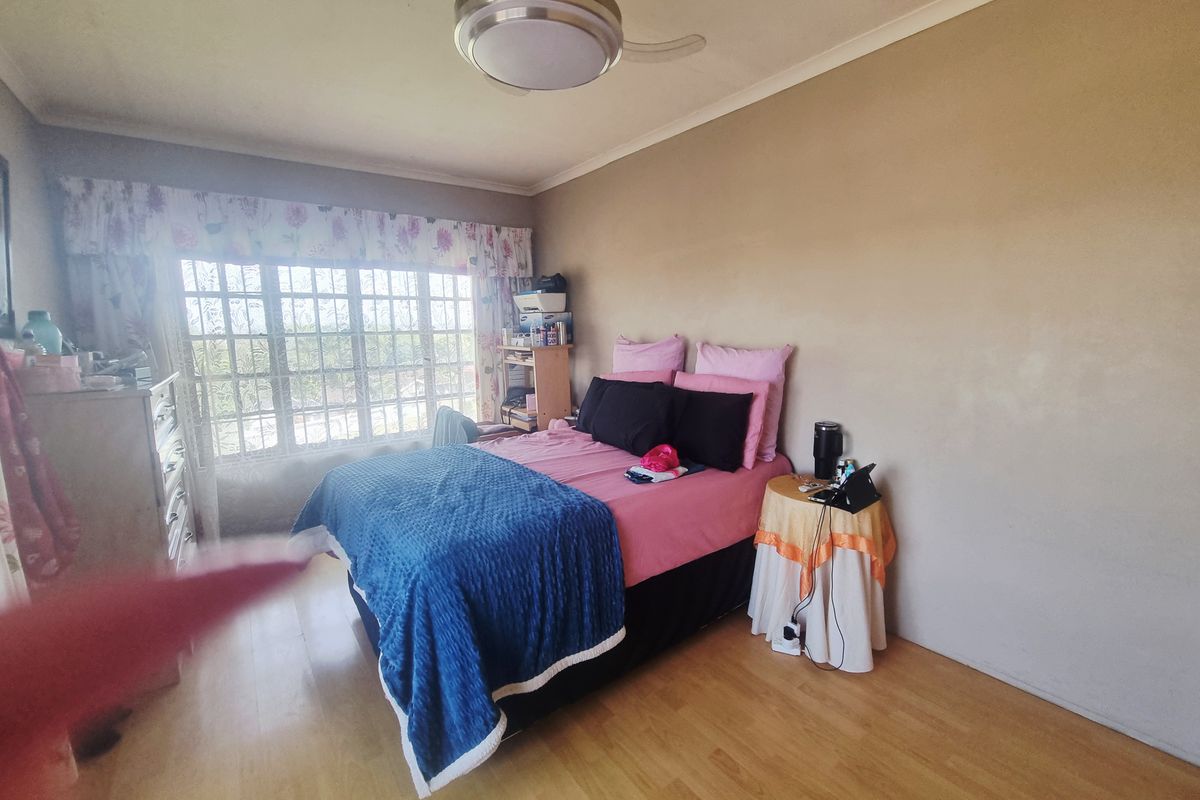 A bedroom featuring laminate flooring, a ceiling fan, and a large window with security bars, offering a functional space for rest.