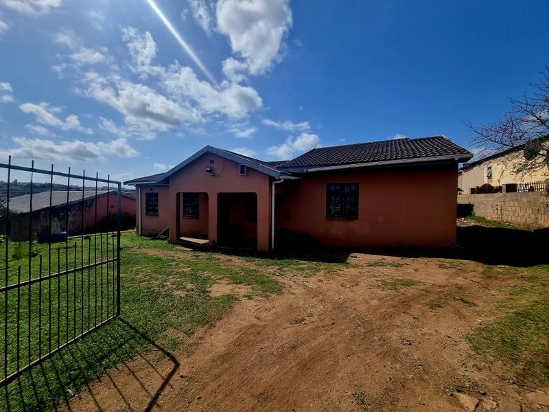 Front view of a single-story detached house featuring a tiled roof, security bars on windows, and an open yard area with a metal entrance gate.