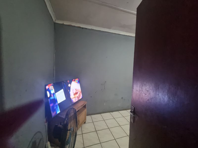 A small living area featuring tiled flooring and coved ceilings, currently showing signs of wear on the walls and ceiling.