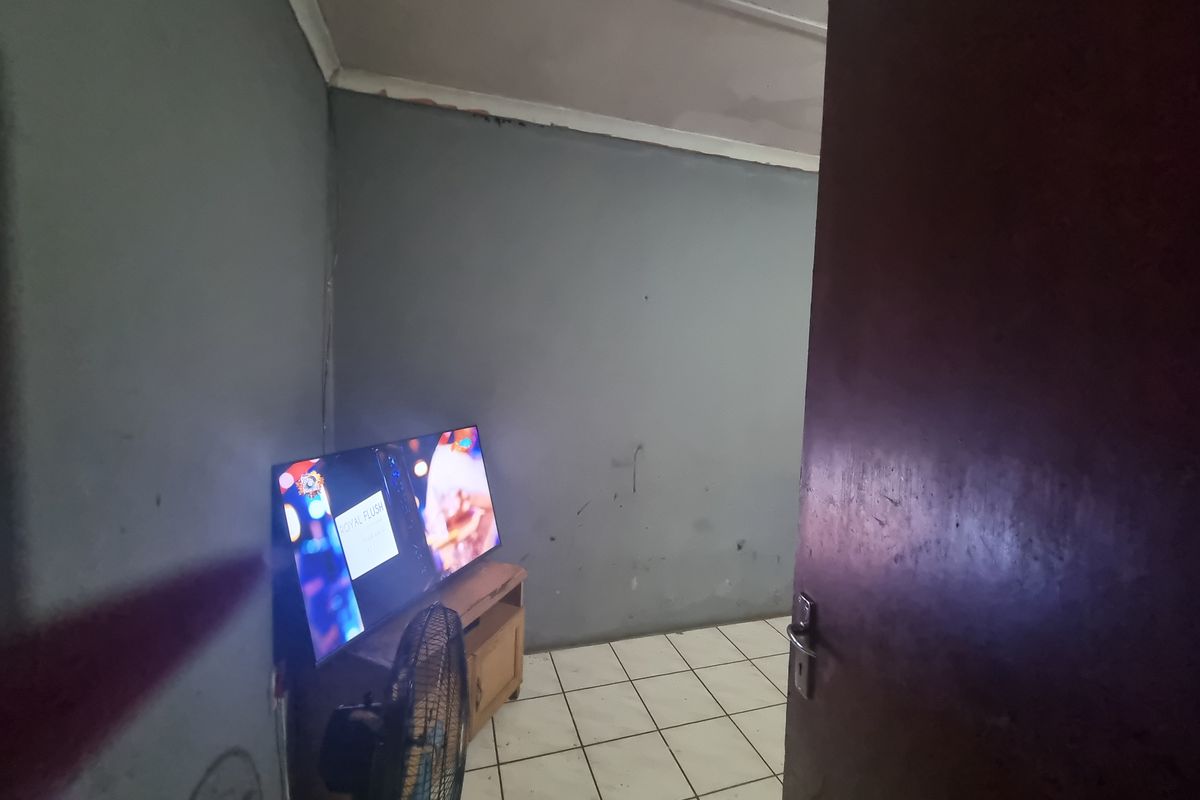 A small living area featuring tiled flooring and coved ceilings, currently showing signs of wear on the walls and ceiling.