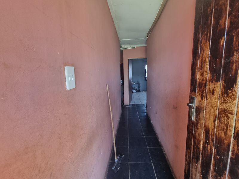 A narrow interior hallway featuring dark tiled flooring and pink painted walls, leading towards an adjacent room.