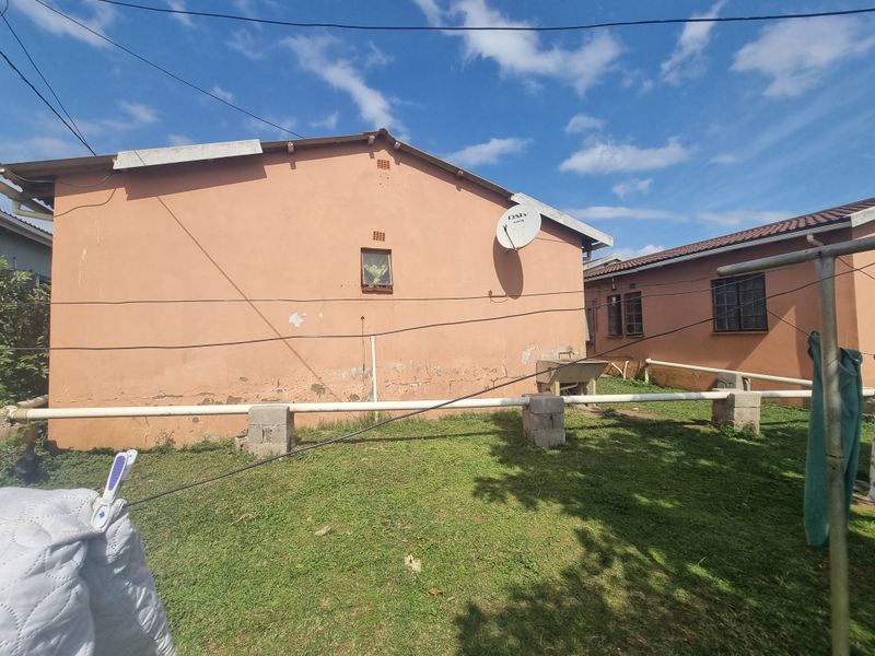 Rear exterior view of the house showing a lawn area, external plumbing, and a concrete laundry basin against the building wall.