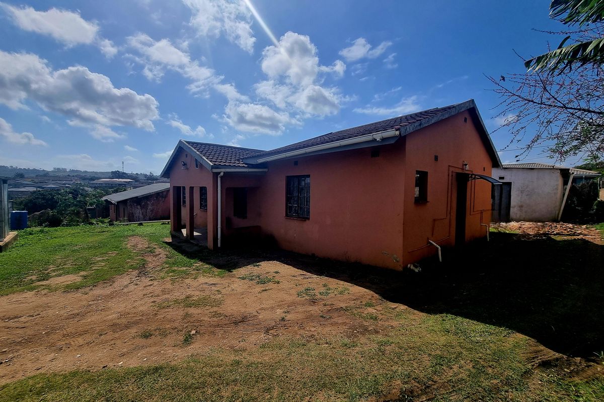 Rear view of a detached house featuring a tiled roof, covered patio area, and surrounding unpaved yard space.