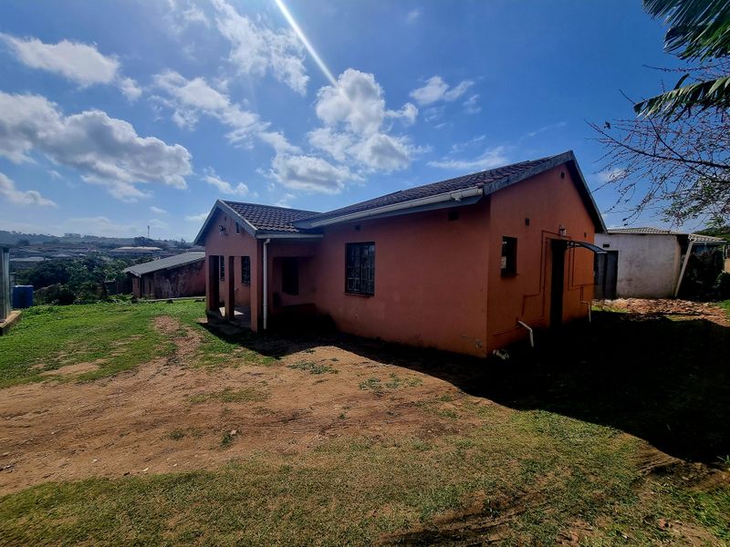 Rear view of a detached house featuring a tiled roof, covered patio area, and surrounding unpaved yard space.