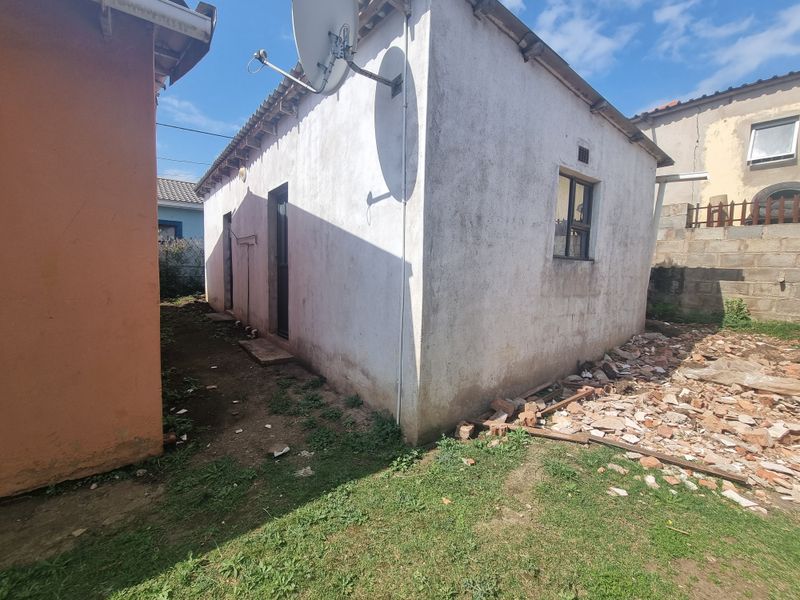Rear exterior view of the property showing the building facade, satellite dish, and surrounding unmaintained yard area with construction debris.