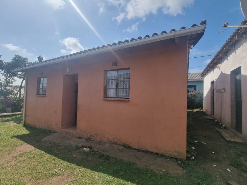 Rear exterior view of a single-story house featuring a tiled roof, gutters, and security-barred windows, showing signs of weathered exterior paint and plaster.