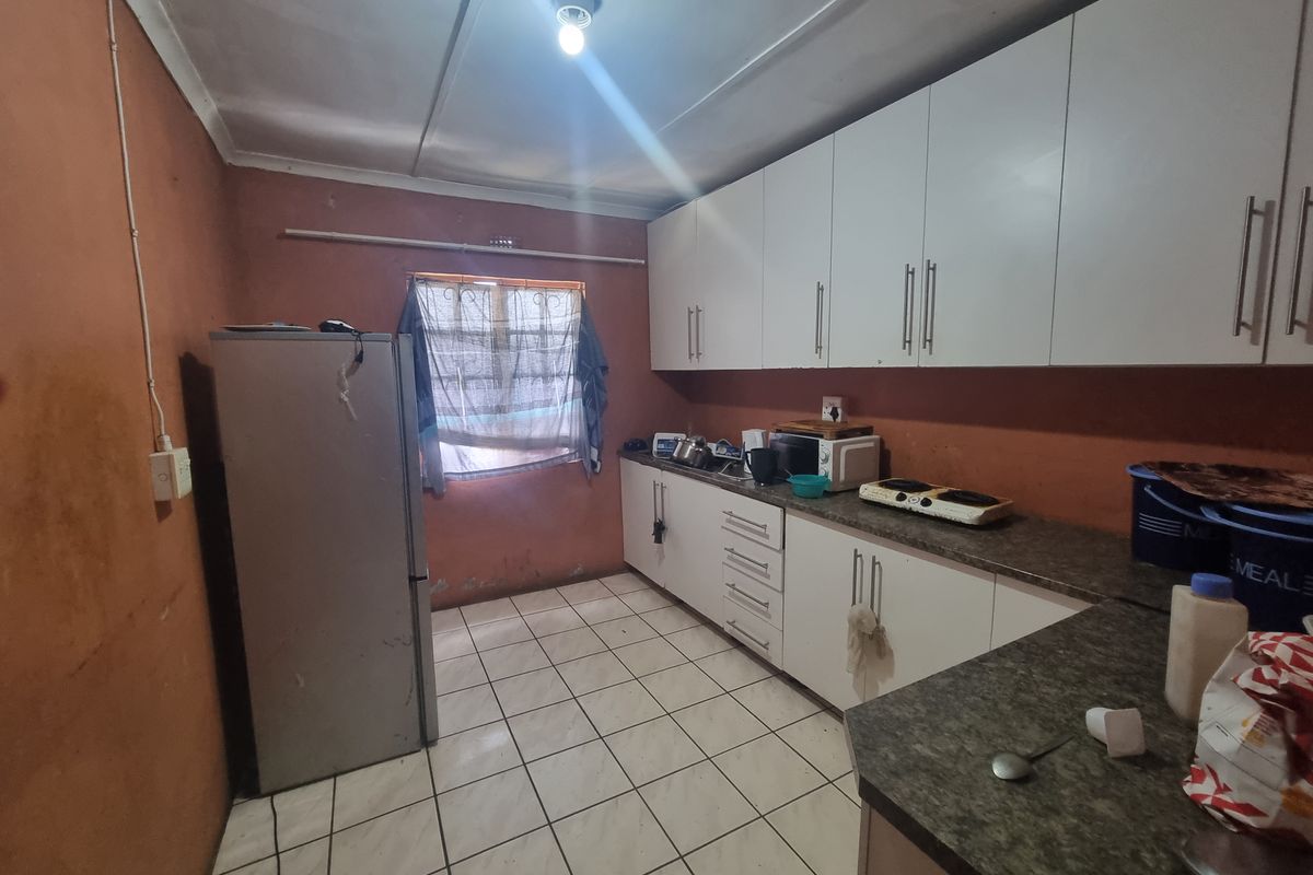 A functional kitchen featuring white built-in cabinetry, laminate countertops, and tiled flooring, requiring cosmetic updates to the wall finishes.