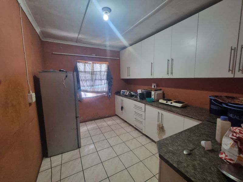 A functional kitchen featuring white built-in cabinetry, laminate countertops, and tiled flooring, requiring cosmetic updates to the wall finishes.