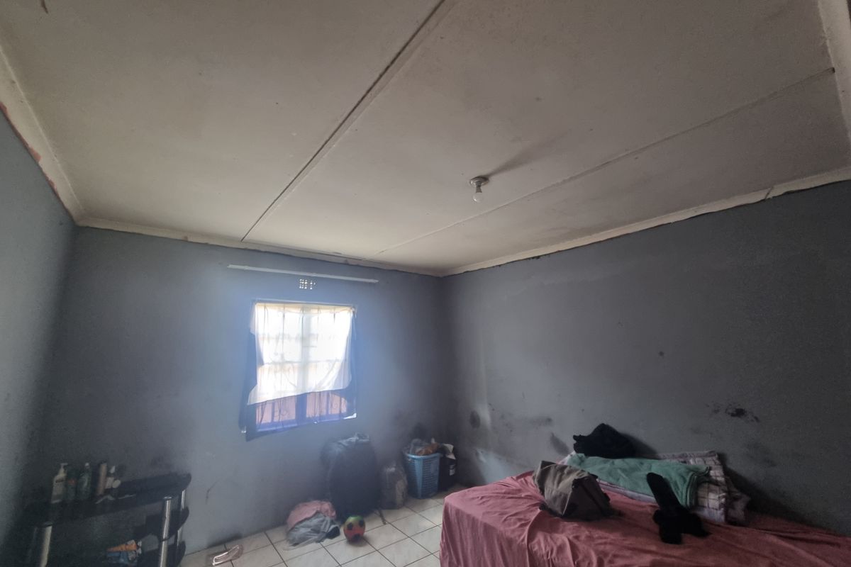 A bedroom featuring tiled flooring and a window, currently showing signs of wear including stained walls and ceiling damage.