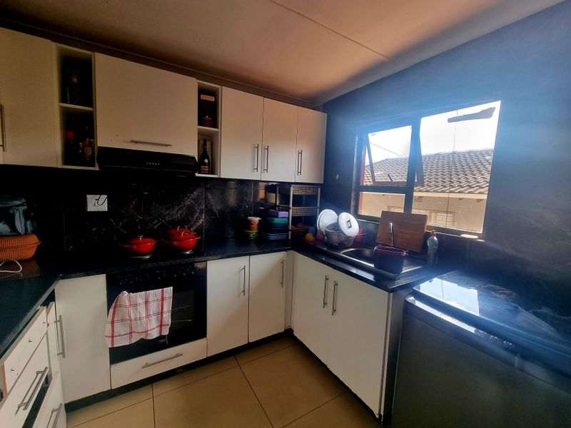 A functional kitchen featuring white cabinetry, dark countertops, a built-in oven with extractor fan, and a stainless steel sink under a window.