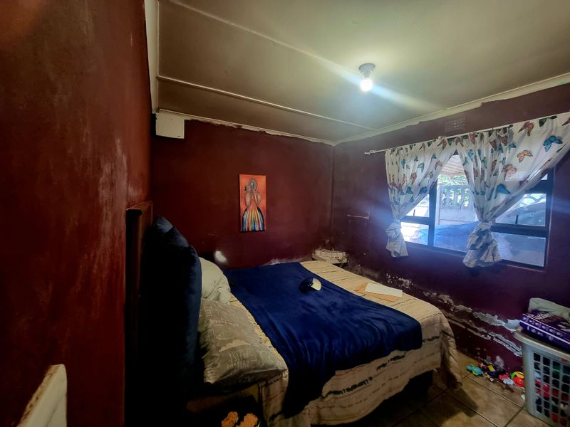 A bedroom featuring tiled flooring and an aluminium window. The walls show significant signs of damp and paint deterioration requiring maintenance.