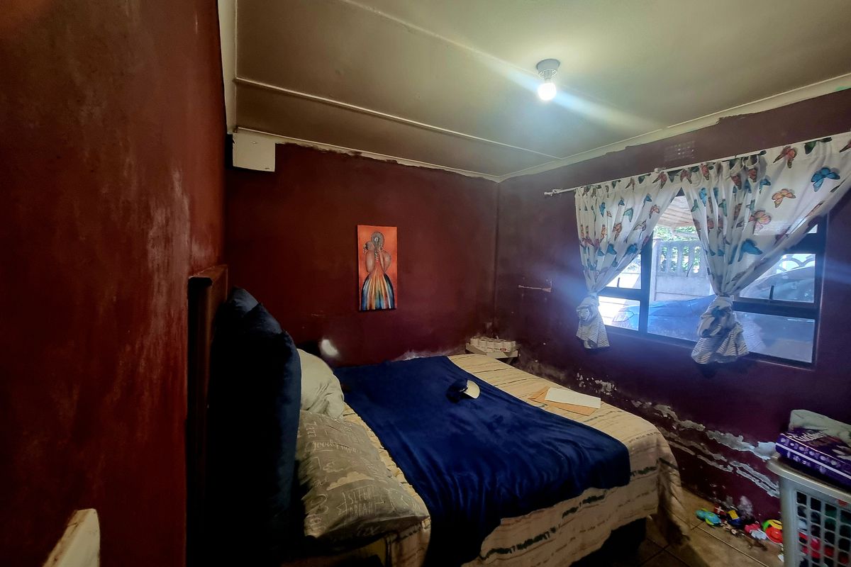 A bedroom featuring tiled flooring and an aluminium window. The walls show significant signs of damp and paint deterioration requiring maintenance.