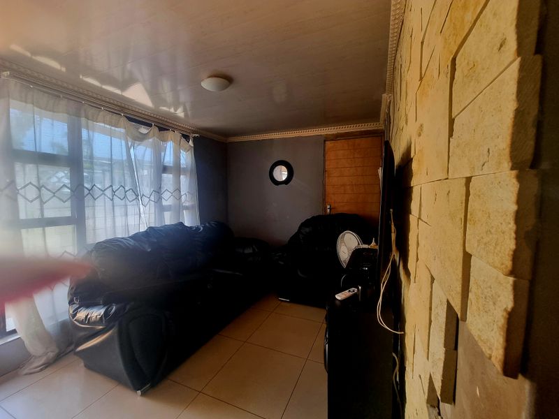Living room featuring a textured stone cladding feature wall, tiled flooring, and large windows allowing natural light.
