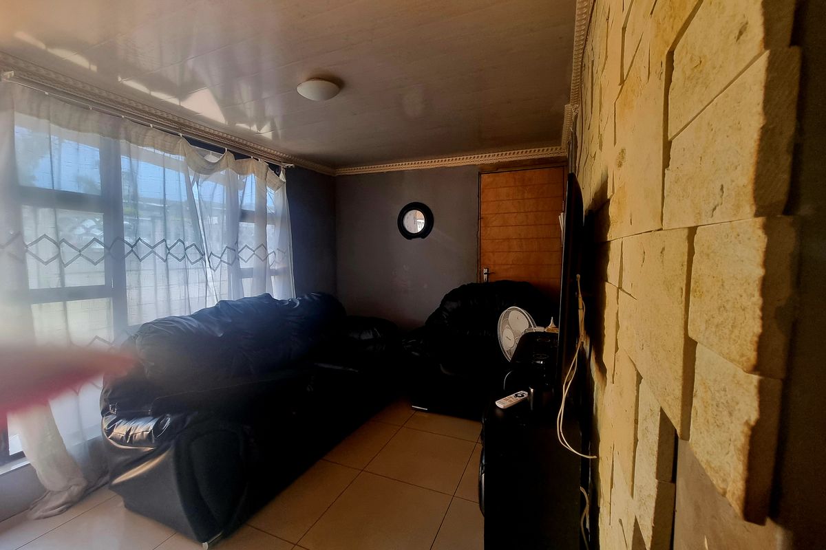 Living room featuring a textured stone cladding feature wall, tiled flooring, and large windows allowing natural light.