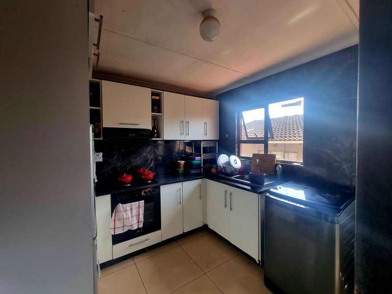 A functional kitchen featuring white cabinetry, dark tiled splashbacks, built-in oven and hob, and tiled flooring with natural light from the window.