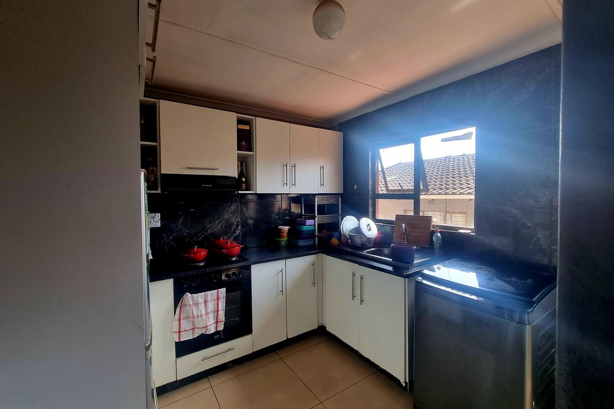 A functional kitchen featuring white cabinetry, dark tiled splashbacks, built-in oven and hob, and tiled flooring with natural light from the window.