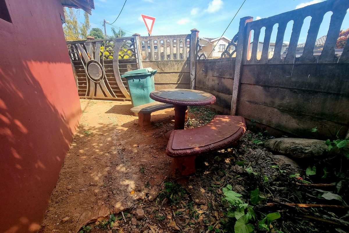 A rear outdoor area featuring a precast concrete boundary wall and metal gate, currently with an unpaved surface and overgrown vegetation.