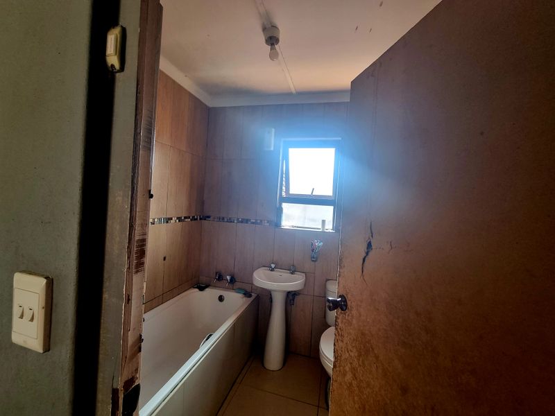 A dated bathroom featuring a pedestal basin, bathtub, and toilet with tiled finishes, requiring cosmetic updates and repairs to the door and frame.