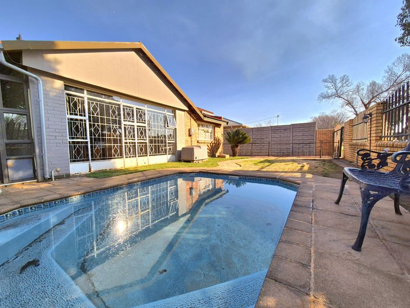 Rear garden area featuring a swimming pool with paved surround, enclosed by a combination of brick and precast concrete boundary walls.