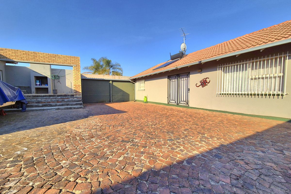 Rear exterior view featuring a large brick-paved courtyard, built-in braai area, and access to the garage, with solar water heating installed on the roof.