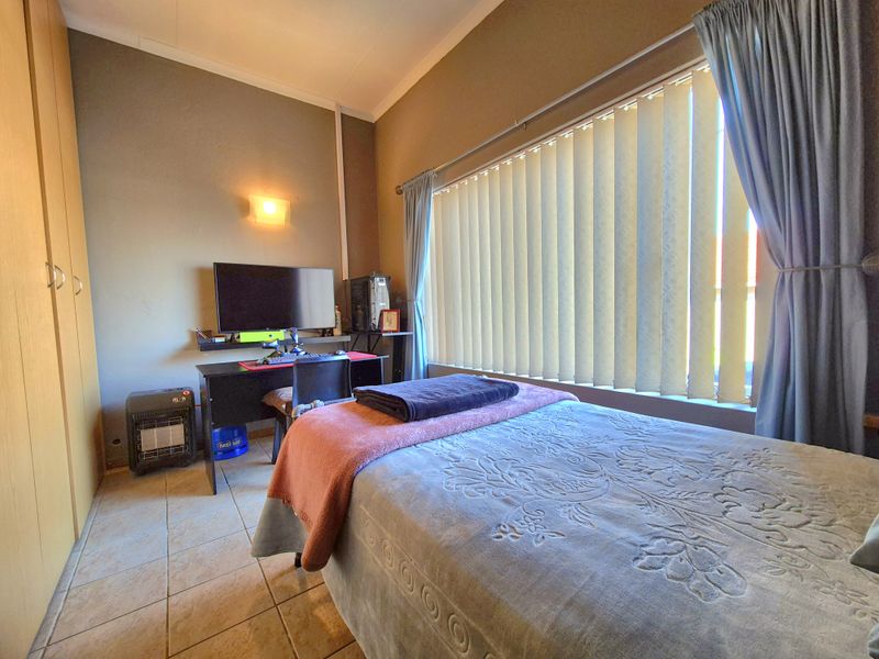 A functional bedroom featuring built-in cupboards, tiled flooring, and large windows with vertical blinds, providing ample natural light.