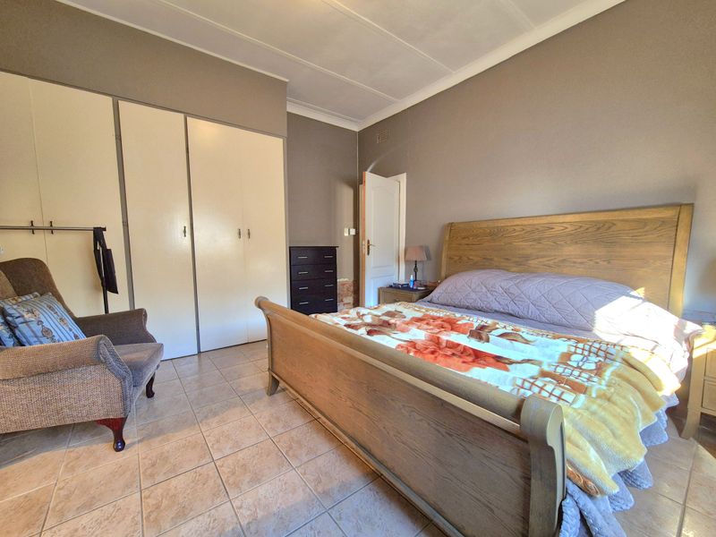 A spacious bedroom featuring tiled flooring, built-in cupboards, and a coved ceiling, offering a functional layout with ample storage space.