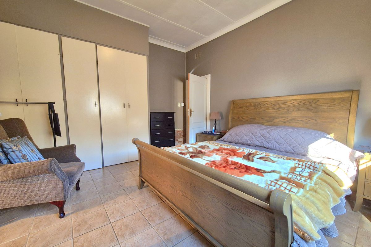 A spacious bedroom featuring tiled flooring, built-in cupboards, and a coved ceiling, offering a functional layout with ample storage space.