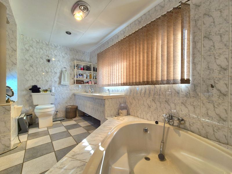 A spacious bathroom featuring a built-in bathtub, dual vanity, and tiled finishes throughout, offering a functional layout with potential for modern updates.