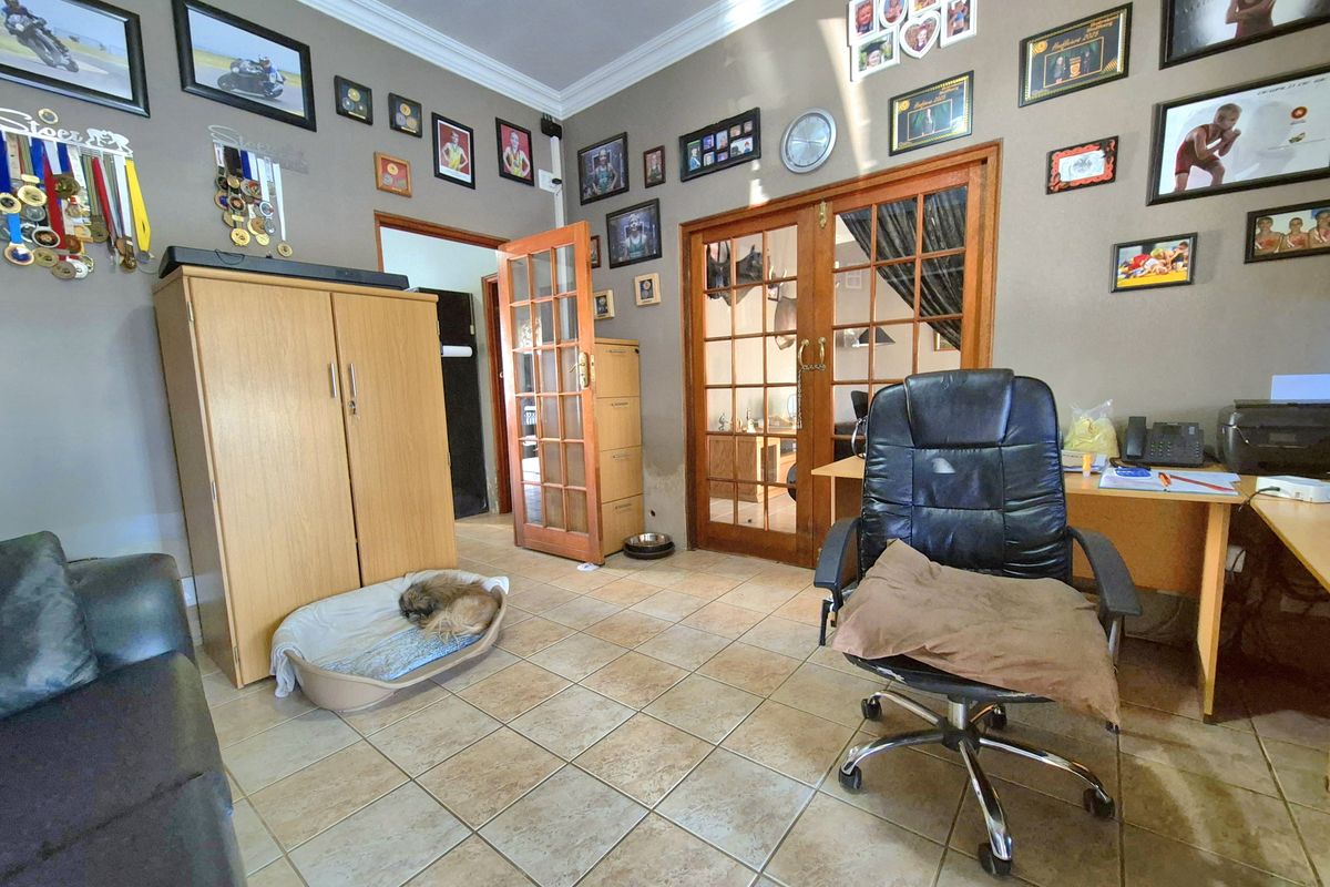 A living area featuring tiled flooring, coving, and wooden french doors leading to an adjacent room, with visible wall staining near the door frame.