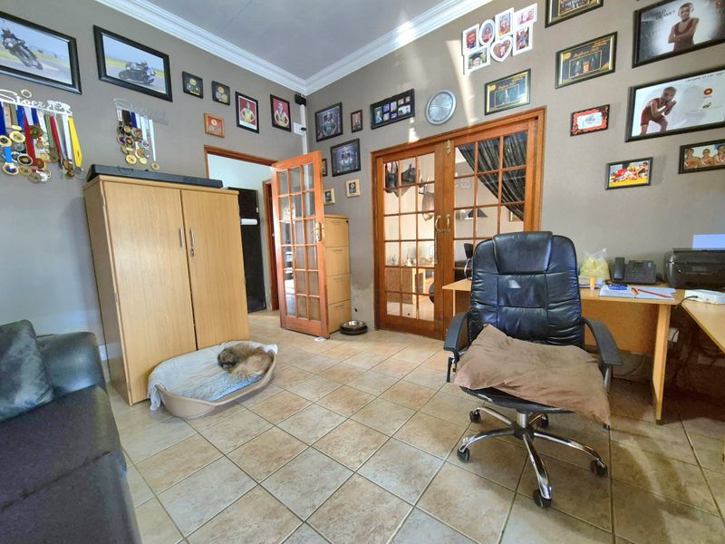 A living area featuring tiled flooring, coving, and wooden french doors leading to an adjacent room, with visible wall staining near the door frame.