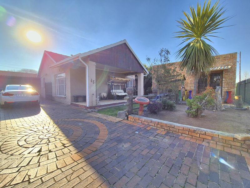 Front view of a single-story house featuring a paved driveway, covered porch, and established garden area with brick retaining walls.
