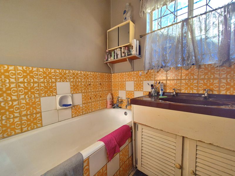 A dated bathroom featuring vintage patterned wall tiles, a built-in vanity cabinet, and a standard bathtub with integrated plumbing fixtures.