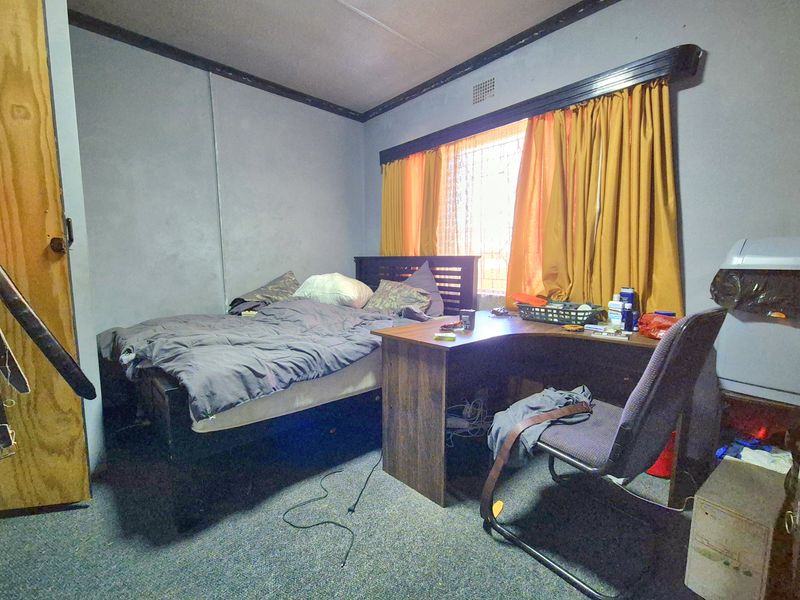 A bedroom featuring carpet flooring and a window with built-in curtain rail, requiring cosmetic updates to wall finishes and trim.