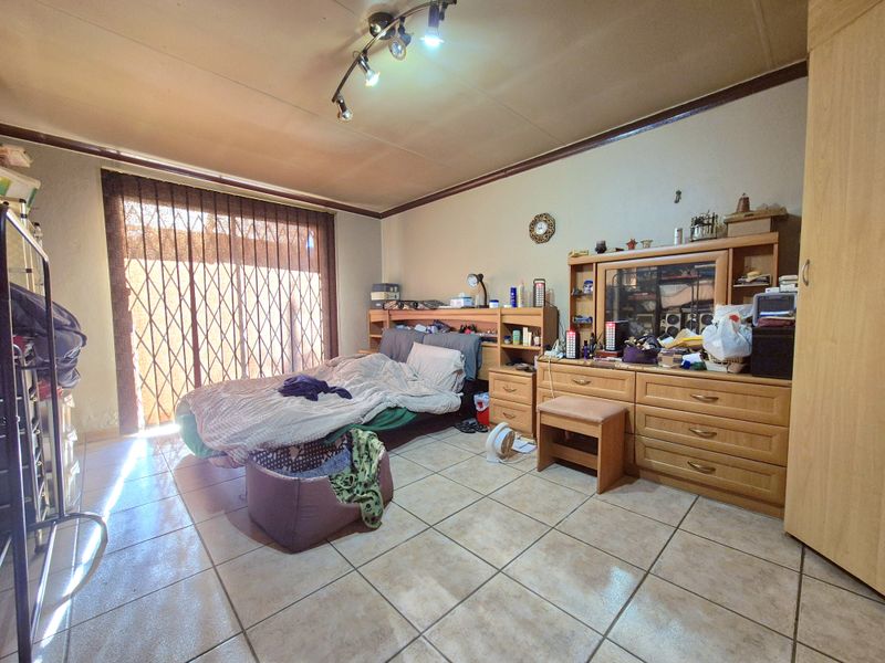 A bedroom featuring tiled flooring, track lighting, and a sliding glass door with an integrated security gate leading to the exterior.