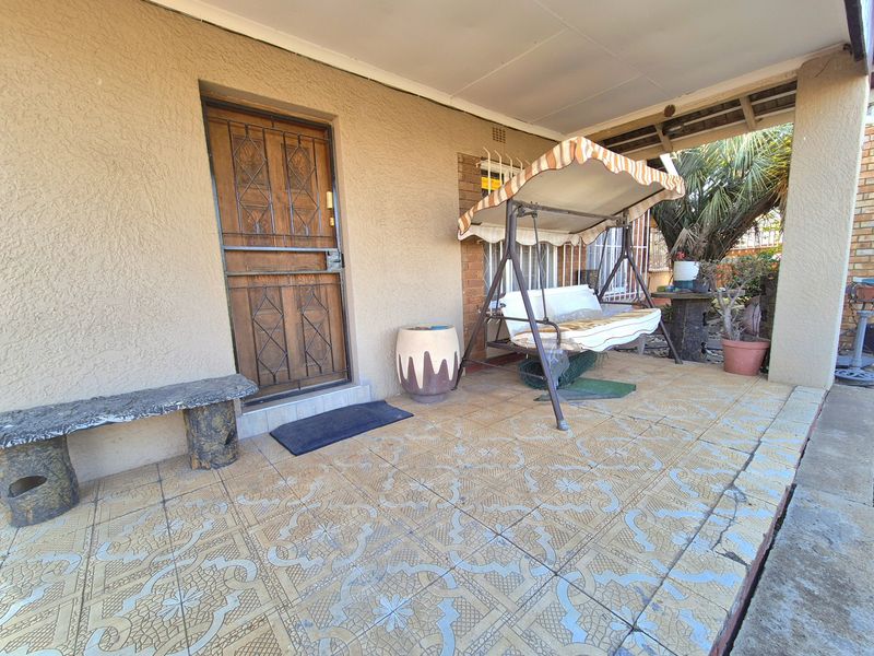 A covered patio area featuring patterned floor tiles, a security gate, and window security bars, providing an outdoor space for relaxation.